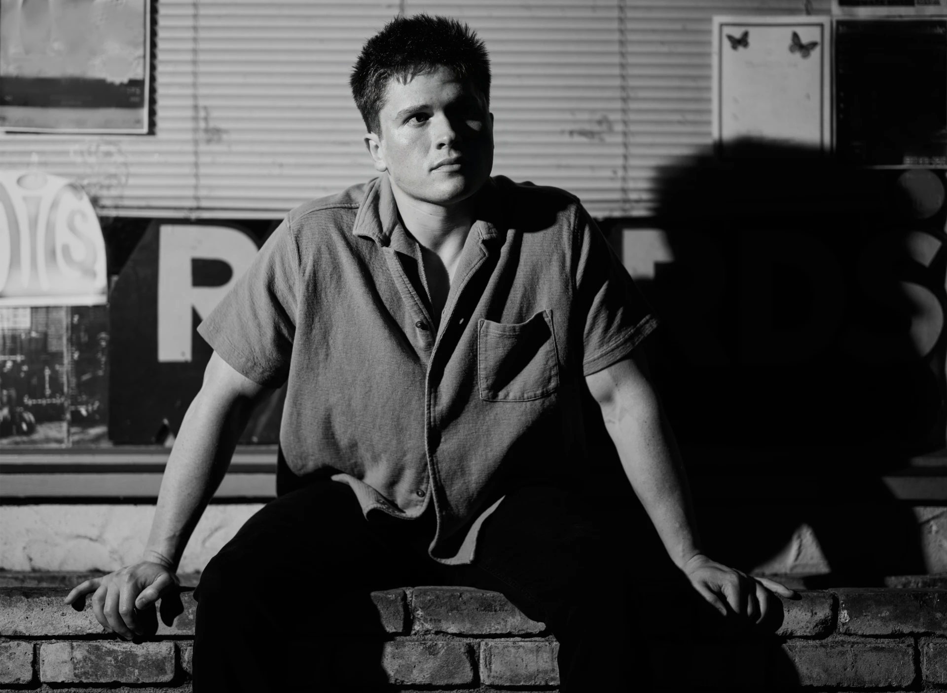 Dramatic black and white nighttime portrait of Jason Kushy sitting on a brick ledge