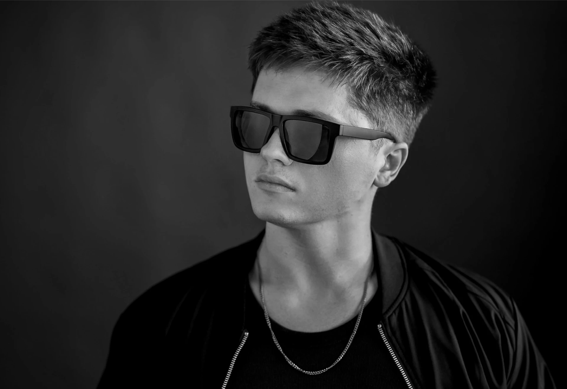 Black and white portrait of Jason Kushy wearing sunglasses and a bomber jacket