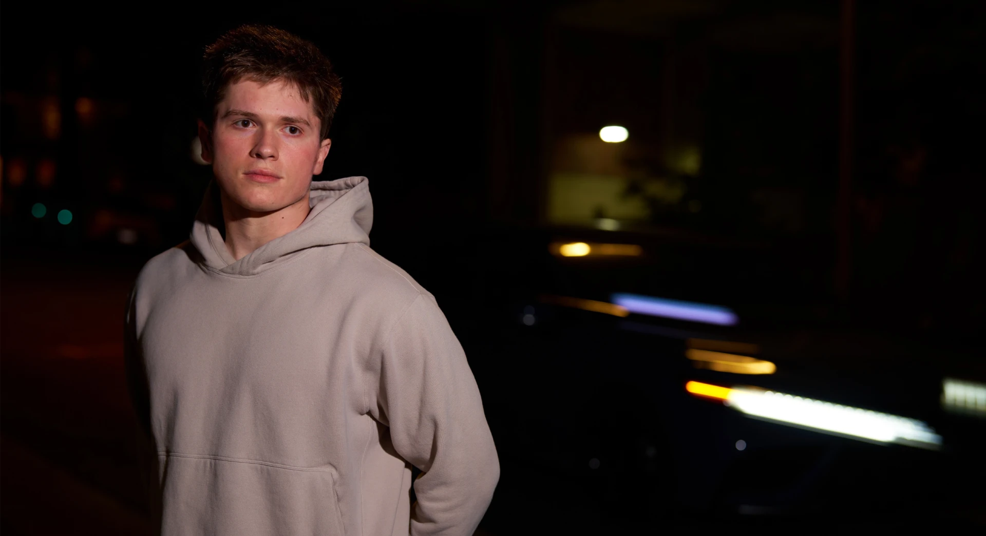 Cinematic nighttime portrait of DJ Jason Kushy in a light hoodie with blurred street lights