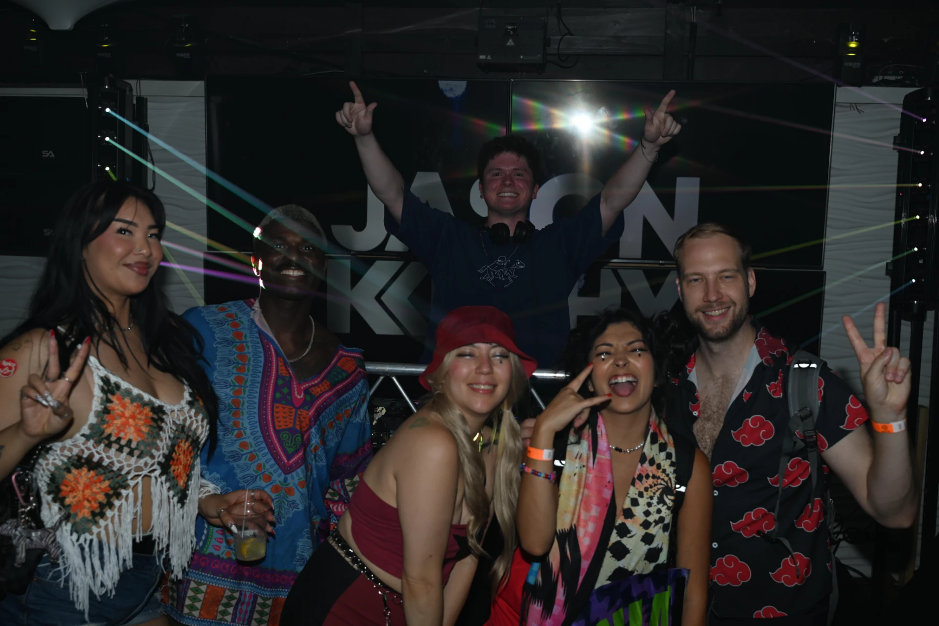 DJ Jason Kushy posing behind his booth with energetic fans at a nightclub performance