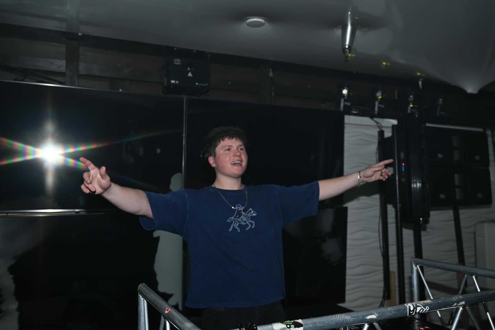 Jason Kushy performing live in the DJ booth with arms outstretched engaging the crowd