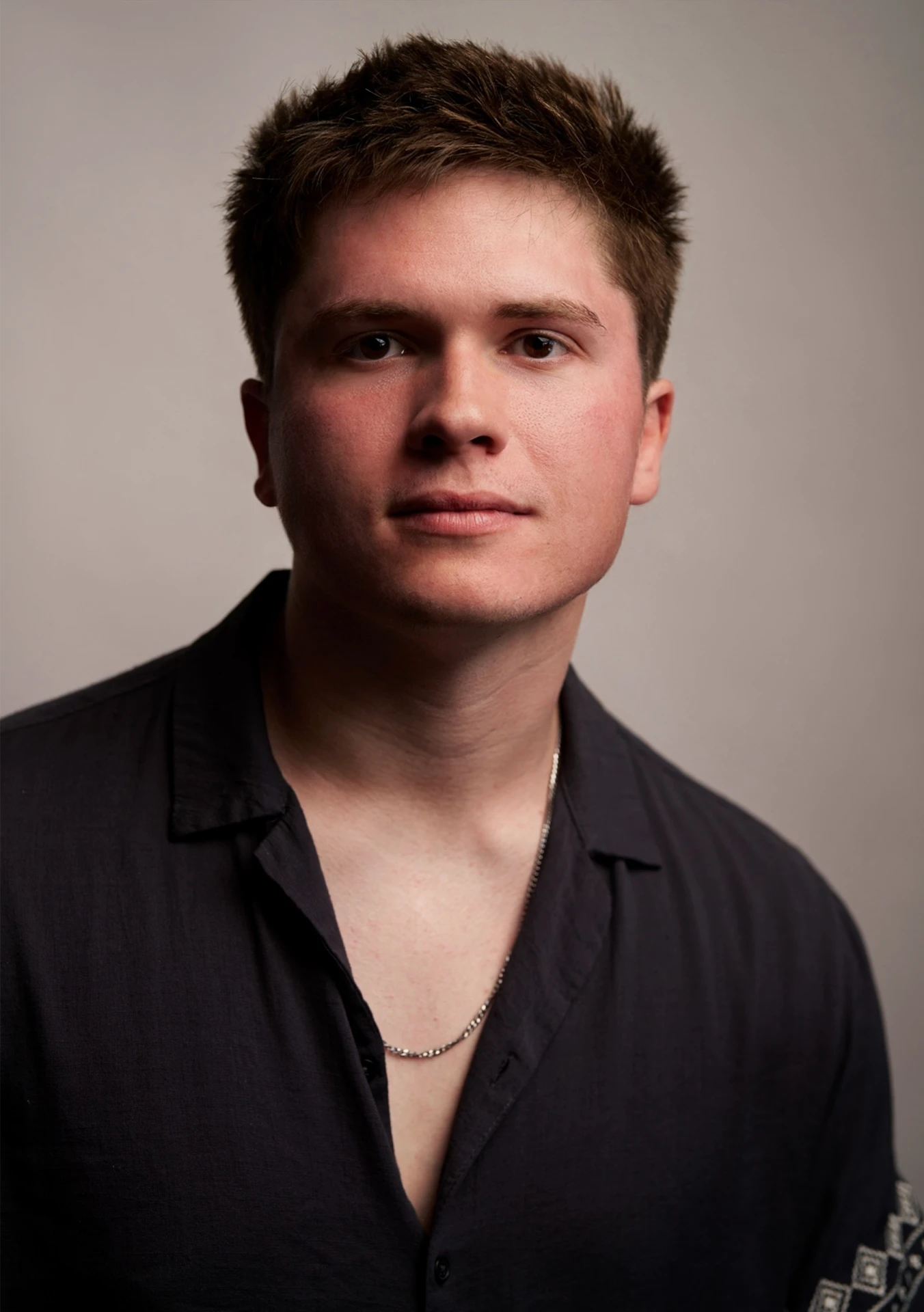 Professional press headshot of Jason Kushy in a black shirt against a grey studio backdrop