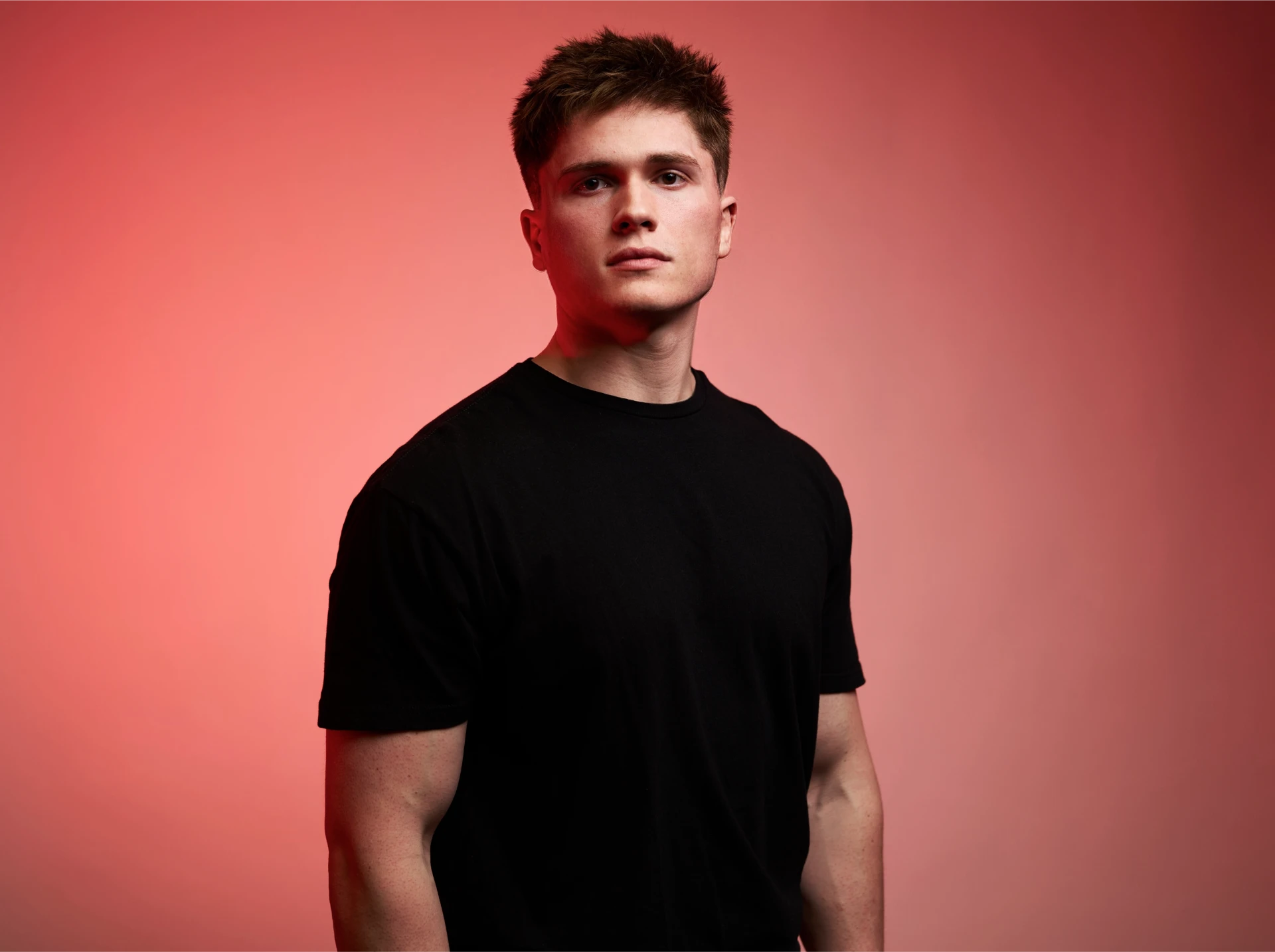 Professional studio portrait of house DJ Jason Kushy in a black t-shirt against a red backdrop